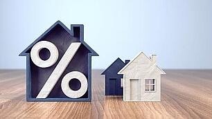 Bauzinsen aktuell Zwei Modellhäuser und auf einem ist ein großes Prozentzeichen zu sehen